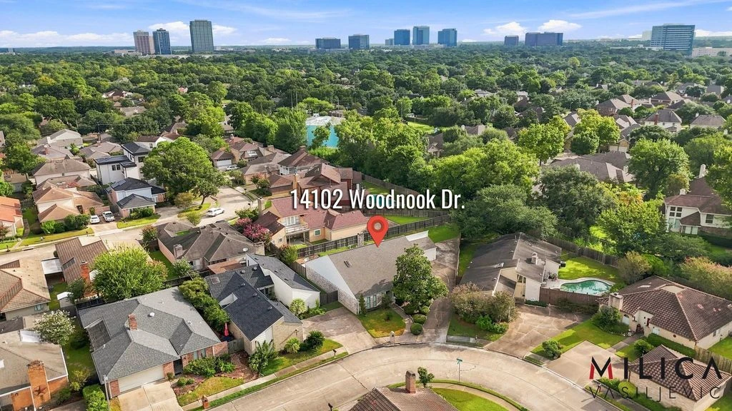 Aerial neighborhood view labeled 14102 Woodnook Dr., with a location pin over the home and trees and buildings in the distance.